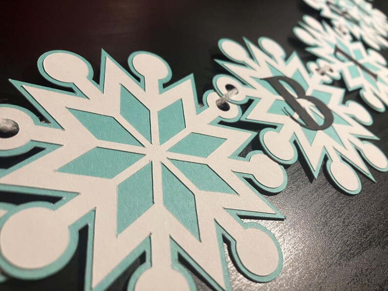 以下が含まれることがあります： 白、水色、黒を基調とした雪の結晶バナー。各雪の結晶は水色の中心部と白い縁取りが施されています。雪の結晶の一つには文字「B」が描かれています。バナーは紐で繋がれています。