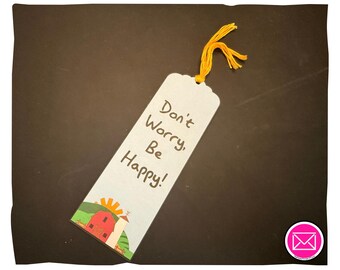 Puede incluir: Un marcapáginas rectangular con fondo claro que presenta el texto "Don't Worry, Be Happy!" en letras de color marrón oscuro. En la parte inferior, una ilustración colorida muestra un granero rojo, colinas verdes y un sol amarillo. Tiene una borla de hilo amarillo.