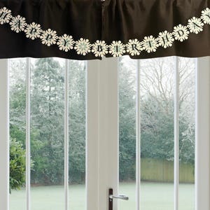 以下が含まれることがあります： 「HAPPY BIRTHDAY」と書かれた装飾的なガーランドが付いた黒い生地のバランス。ガーランドには白と水色の雪の結晶の切り抜きがあります。バランスは、緑の庭と木々が見えるガラスドアの上に吊り下げられています。