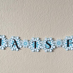 以下が含まれることがあります： 「AMELIA IS FOUR!!!」と書かれた、雪の結晶型の切り抜きで作られたバナー。雪の結晶は白と水色のアクセントと中心のデザイン。文字は黒色です。