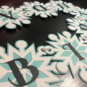 以下が含まれることがあります： 白、水色、黒を基調とした雪の結晶バナー。各雪の結晶は水色の中心と黒い文字が特徴です。バナーは白い紐で繋がれています。