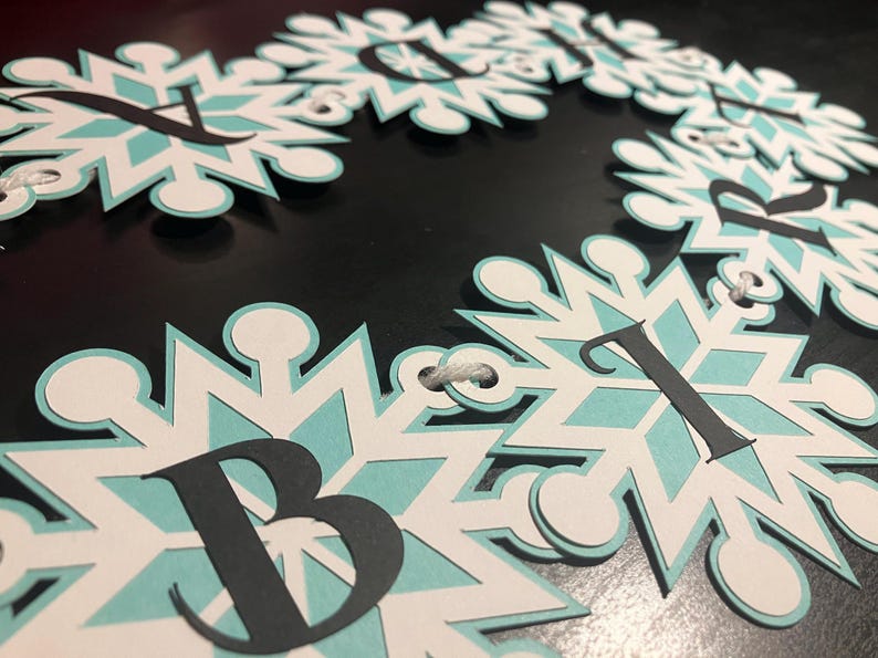 以下が含まれることがあります： 白、水色、黒を基調とした雪の結晶バナー。各雪の結晶は水色の中心と黒い文字が特徴です。バナーは白い紐で繋がれています。