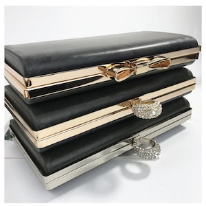 May include: A black clutch purse with a gold and silver clasp. The clasp is decorated with a bow and a ring of rhinestones.