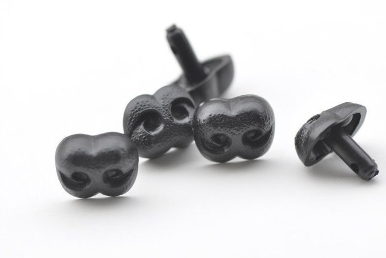 K&ouml;nnte beinhalten: Vier schwarze Plastik-Spielzeugnasen mit einer strukturierten Oberfl&auml;che und zwei L&ouml;chern. Die Nasen haben einen kleinen Stift auf der R&uuml;ckseite zum Befestigen.