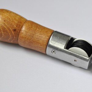 May include: A wooden handled leather stitching tool with two spools of black thread.
