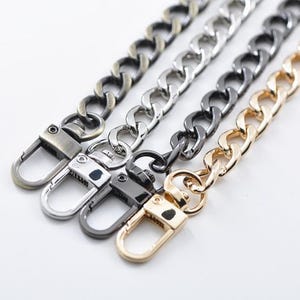 Puede incluir: Cuatro cadenas de eslabones de metal dispuestas en paralelo, cada una con un cierre de mosquetón en el extremo. Los acabados incluyen latón antiguo, plata pulida, metal gris oscuro y oro brillante, con un diseño de eslabones entrelazados.