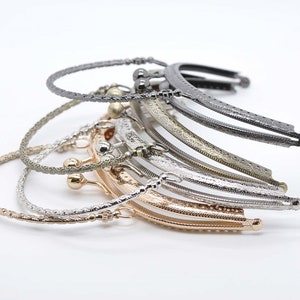 May include: A stack of six different metal purse frames. The frames are in various finishes, including silver, gold, and black. The frames are all in the shape of a half-circle and have a decorative design.