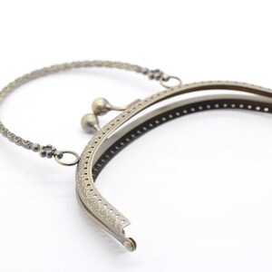 May include: A gold-toned metal purse frame with a decorative handle and a snap closure. The frame is designed to be used for crafting purses and bags.