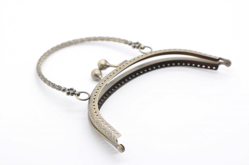 May include: A gold-toned metal purse frame with a decorative handle and a snap closure. The frame is designed to be used for crafting purses and bags.