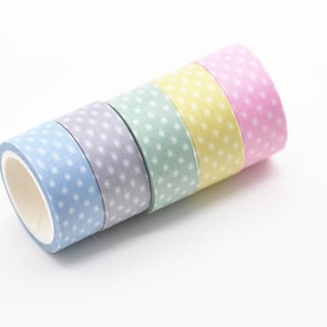 May include: Five rolls of washi tape in pastel shades of blue, lilac, mint green, yellow, and pink. Each roll features small white polka dots. The tape is arranged diagonally on a white background.