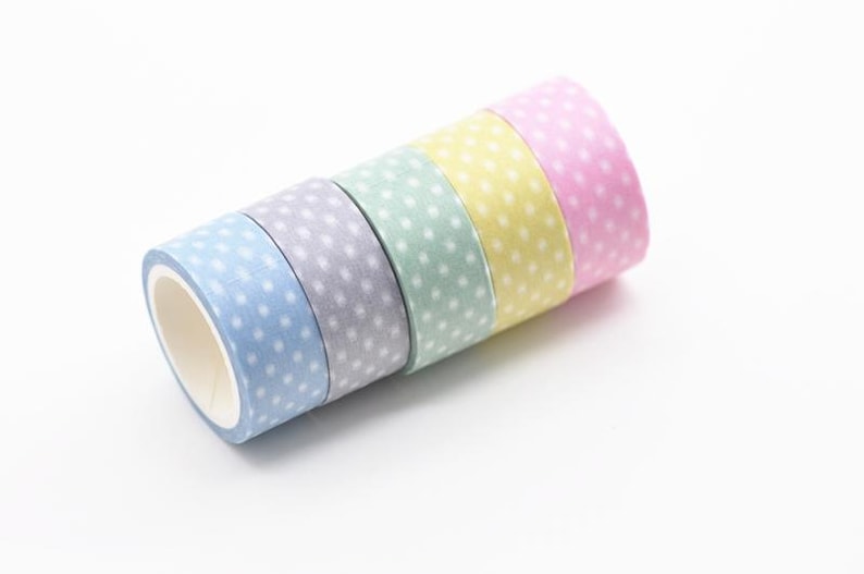 May include: Five rolls of washi tape in pastel shades of blue, lilac, mint green, yellow, and pink. Each roll features small white polka dots. The tape is arranged diagonally on a white background.