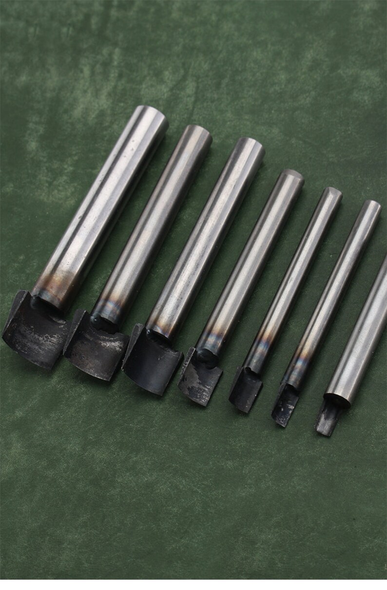 May include: Set of seven metal leather hole punches with different sizes. The punches are silver and have a rounded edge.