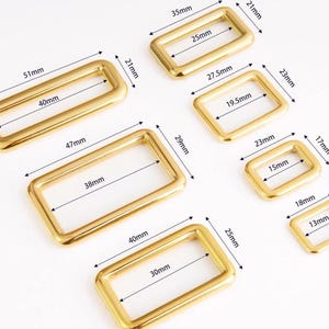 Può includere: Una collezione di anelli rettangolari in metallo dorato di varie dimensioni. Le misure in millimetri sono indicate per ogni anello, con il più grande di 51 mm di lunghezza e il più piccolo di 13 mm. Adatto per l'artigianato.