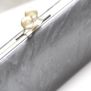 May include: A silver clutch bag with a silver clasp and two pearl-like embellishments.
