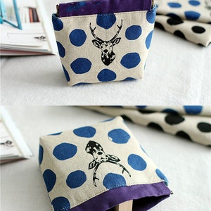 May include: Two small, beige fabric pouches with blue polka dots and a black deer silhouette. The pouches have a purple fabric trim and are folded open to show the inside.