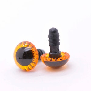 May include: Two orange plastic safety eyes with black pupils and a black plastic washer. The eyes have a textured, wavy rim.