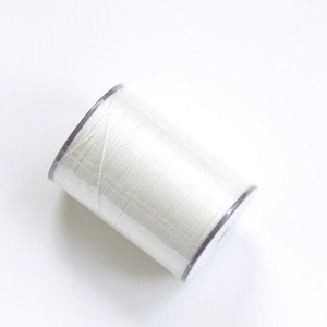 May include: A spool of white thread wrapped in clear plastic.