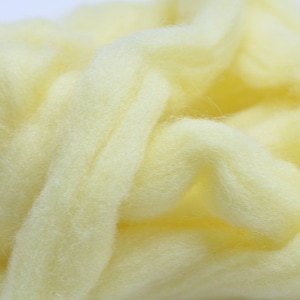 May include: A close-up of a pile of pale yellow wool roving. The wool is soft and fluffy, and it is perfect for spinning or felting.