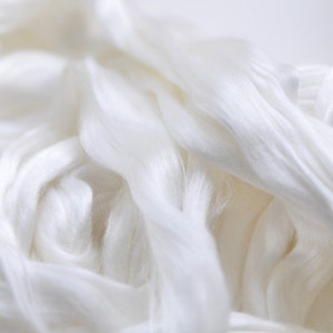 May include: Close-up of a pile of white silk fibers. The fibers are soft and flowing, with a subtle sheen. The image highlights the texture and delicate nature of the material, suggesting its use in textiles or crafting.