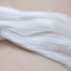May include: Close-up of a bundle of soft, white fiber. The fibers are layered and appear to be smooth and delicate, with a slight sheen. The texture suggests a natural material, possibly silk or wool.