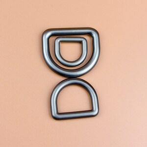 May include: Three black metal D-rings of different sizes. The rings are stacked on top of each other.
