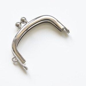 Könnte beinhalten: Silberfarbener Metallrahmen für eine Handtasche mit zwei runden Dekorkugeln oben.