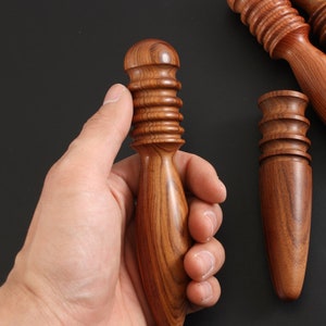 May include: A wooden massage tool with a rounded, textured head and a pointed tip. The tool is made of dark brown wood with a natural grain pattern.
