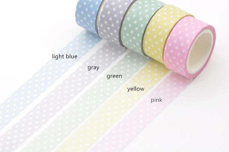 May include: A selection of washi tape rolls in light blue, grey, green, yellow, and pink. Each roll has a polka dot design. The tape is unrolled, showing the colours and patterns.