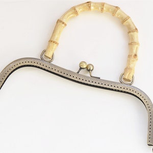 May include: A metal purse frame with a bamboo handle. The frame is antique brass in color and has a decorative pattern. The handle is natural in color and is made of multiple pieces of bamboo.