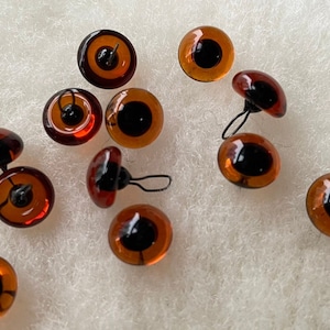 May include: A group of 11 brown glass safety eyes with black pupils and metal loops for attaching to a craft project.