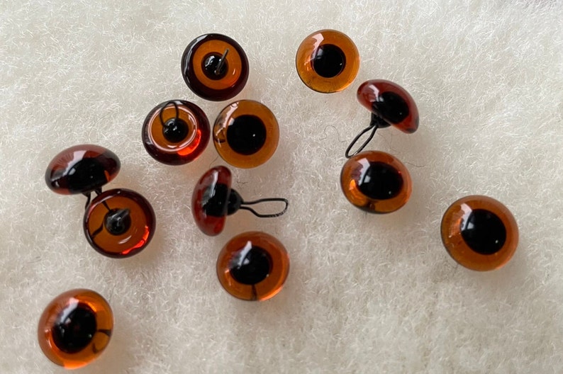 May include: A group of 11 brown glass safety eyes with black pupils and metal loops for attaching to a craft project.