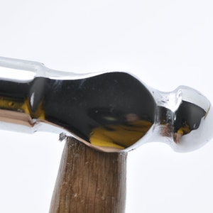 May include: A silver-colored hammer with a wooden handle. The hammer has a rounded head and a smooth, polished surface.