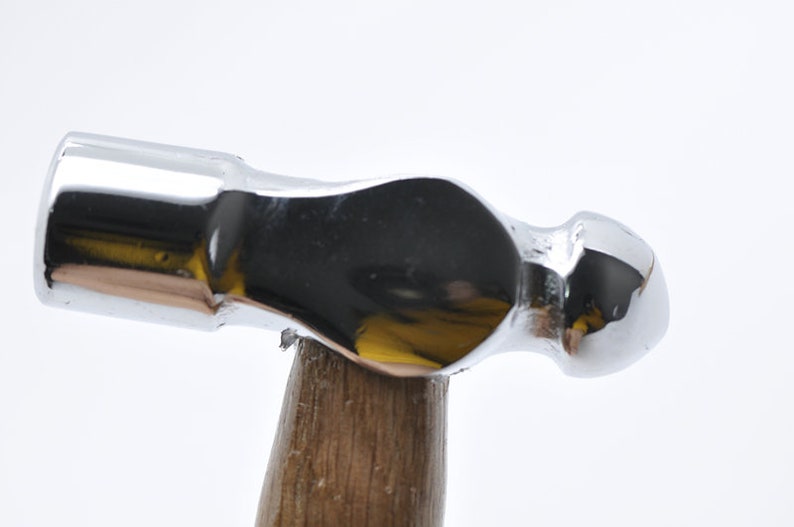 May include: A silver-colored hammer with a wooden handle. The hammer has a rounded head and a smooth, polished surface.