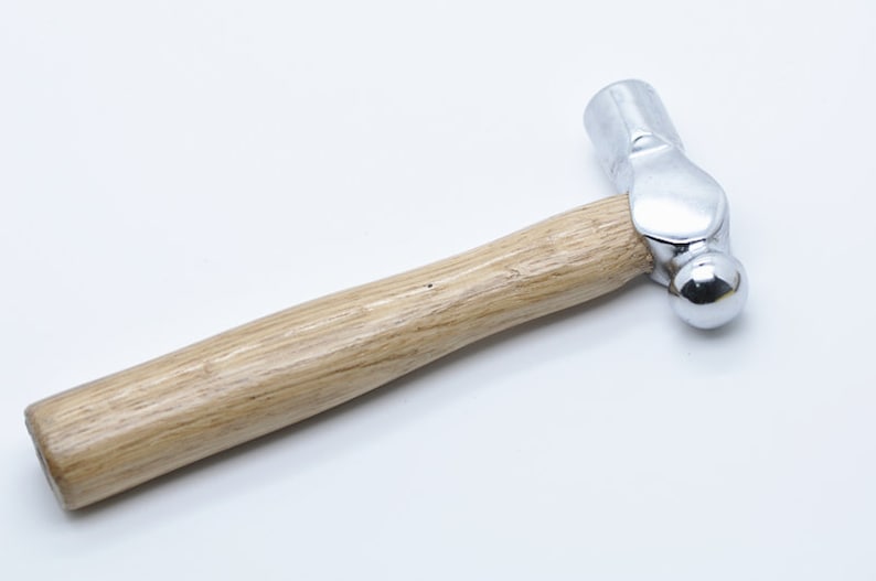 May include: A ball-peen hammer with a wooden handle. The hammer head is silver and the handle is a light brown color.