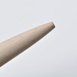 May include: Close-up of the tip of a wooden dowel rod. The rod is light brown and has a smooth, rounded end.