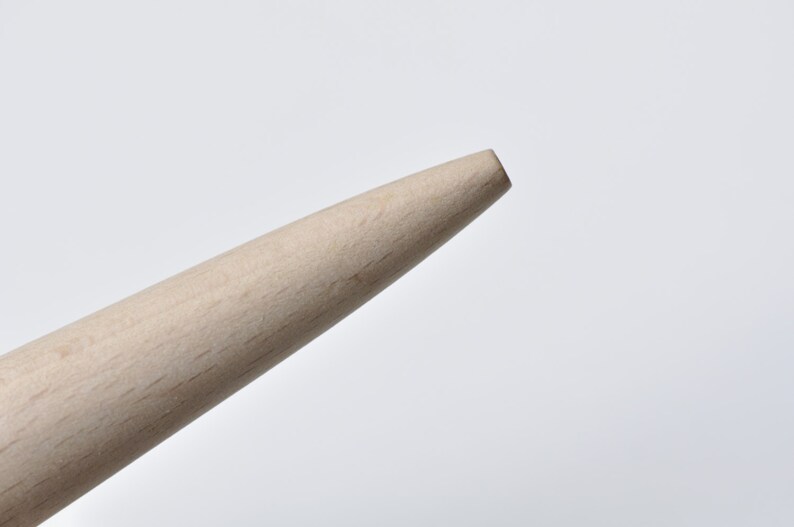 May include: Close-up of the tip of a wooden dowel rod. The rod is light brown and has a smooth, rounded end.