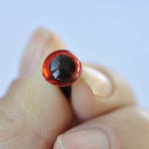 Puede incluir: Un solo ojo de seguridad de pl&aacute;stico rojo con pupila negra, utilizado para manualidades y la fabricaci&oacute;n de mu&ntilde;ecas.