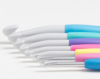 May include: A set of six crochet hooks with colorful handles. The hooks are made of white plastic and have silver metal tips. The handles are blue, turquoise, purple, yellow, and pink.