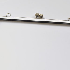May include: A silver-toned metal purse frame with two round metal clasps at the top.