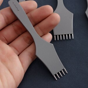 May include: A set of four gray leather hole punches with a silver metal tip. The punches are labeled with the size "4.0MM".