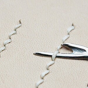 May include: A close-up of a silver leather stitching tool used to separate and push apart stitches in leather goods.