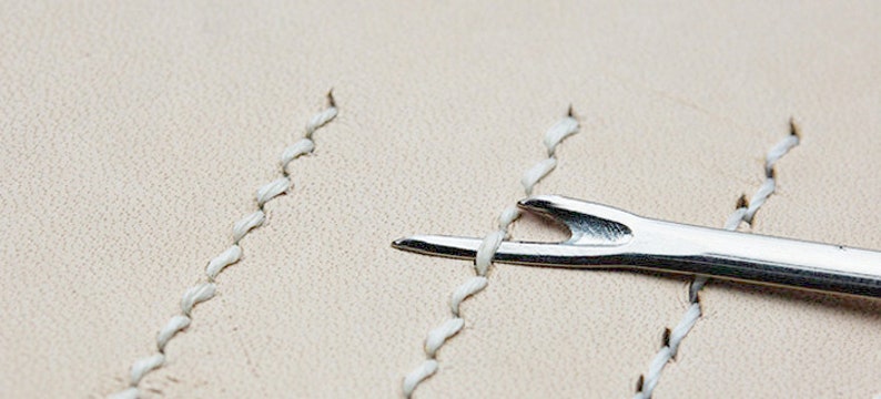 May include: A close-up of a silver leather stitching tool used to separate and push apart stitches in leather goods.