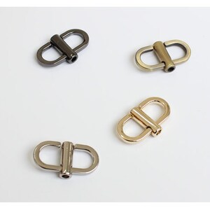 May include: Four metal D-ring clasps in different finishes: silver, gold, black, and antique brass. These clasps are commonly used for attaching straps or chains to bags, purses, or other accessories.