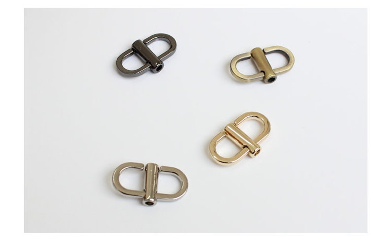 May include: Four metal D-ring clasps in different finishes: silver, gold, black, and antique brass. These clasps are commonly used for attaching straps or chains to bags, purses, or other accessories.