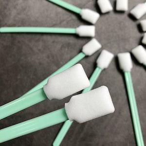 Könnte beinhalten: Nahaufnahme von zwei Tupfern mit grünem Griff und weißen Schaumstoffspitzen. Die Tupfer sind sternförmig angeordnet, mit anderen Tupfern im Hintergrund.
