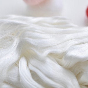 May include: Close-up of a pile of white silk fibers. The fibers are soft and flowing, with a slight sheen. The image is well-lit, highlighting the texture and color of the silk. The background is blurred, focusing attention on the silk.