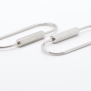 May include: Two silver keychains with a cylindrical bar in the middle. The keychains are oval shaped and have a smooth finish.