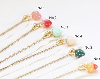 May include: Close-up of six white zippers with gold-colored metal teeth and pulls. Each pull is adorned with a different colored, strawberry-shaped bead. The beads are pink, red, mint green, cream, dark green, and orange-red.