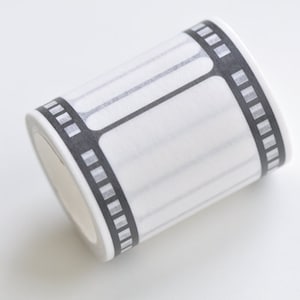 May include: A roll of white washi tape with a black film strip design. The tape features rectangular frames and a dotted border, perfect for crafting and journaling projects. The tape is on a white background.