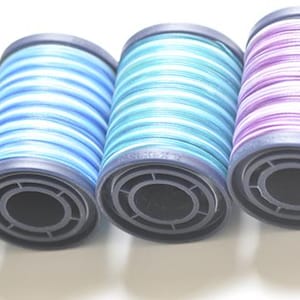 May include: Five spools of thread in a row, featuring green, blue, teal, purple, and green. Each spool has a black base and is filled with tightly wound thread, creating a striped effect. Suitable for sewing and craft projects.